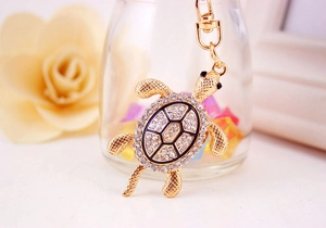 Détail d'un porte-clés tortue dorée avec strass scintillants et motifs en émail noir