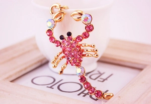 Detail of cute scorpion keychain with rose rhinestones resting on a white ceramic cup