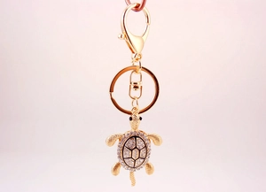Vue macro du porte-clés tortue dorée orné de strass blancs et d'un anneau métallique