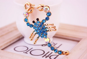 Detail of a golden scorpion keychain featuring blue rhinestones and crystal accents
