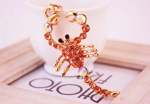 Detail of a golden scorpion brooch with orange rhinestones resting on a white ceramic cup