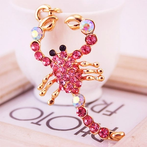 Golden scorpion keychain with pink rhinestones and white crystals on a white ceramic cup