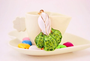 Detail of flower keychain with white enamel petals and green rhinestones on gold metal