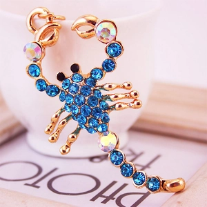 Golden scorpion pendant keychain with sparkling deep blue rhinestones on a ceramic cup