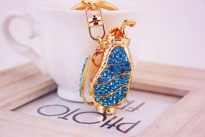Détail d'un porte-clés sac de golf en métal doré orné de strass bleus étincelants