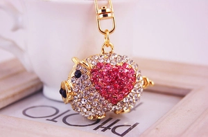 Détail d'un porte-clés cochon doré avec cœur en strass rose sur cadre en bois