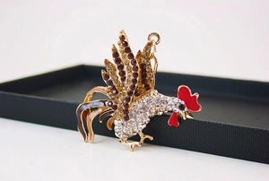 Détail d'un porte-clés coq doré serti de strass présenté sur un coffret cadeau noir