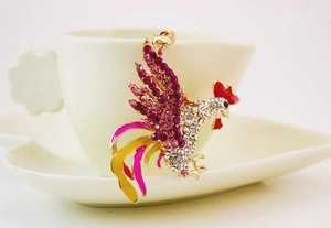 Vue macro d'un porte-clés coq en strass avec cristaux roses sur une tasse en céramique blanche