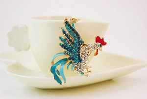 Détail d'un porte-clés coq en strass bleu avec finition dorée sur une tasse blanche