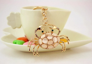 Detail of a golden crab keychain with cat eye stones and green gems near a coffee cup