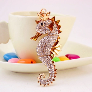 Golden seahorse keychain with white rhinestones and crown, leaning on a white cup
