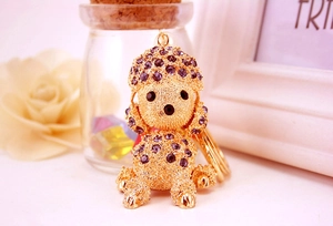 Detail of a golden poodle keychain encrusted with purple crystals on a soft pink background