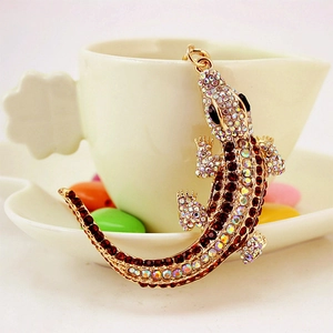 Lizard keychain with sparkling rhinestones on golden metal base resting on white cup