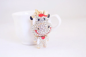 Détail d'un porte-clés vache doré orné de cristaux blancs et d'émail rouge