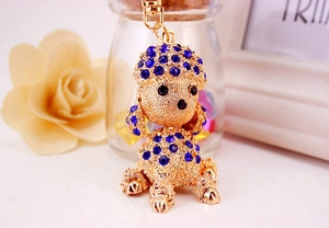 Detail of golden poodle keychain with blue rhinestones and textured metal surface