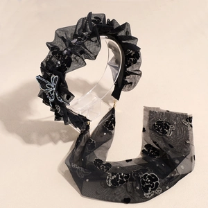 Détail d'un serre-tête en dentelle noire avec motifs roses et charm papillon brillant