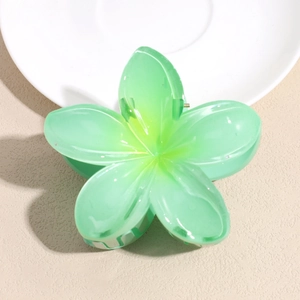 Detail view of a translucent green plumeria flower hair claw clip on a white ceramic plate