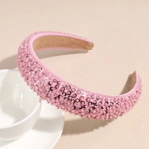 Serre-tête rose à paillettes avec perles et strass sur un fond beige chaleureux