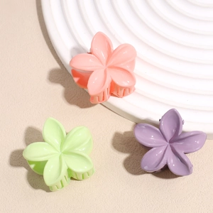 Trois pinces à cheveux fleurs mates en rose, vert et violet sur une assiette blanche