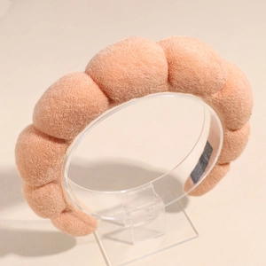 Détail du serre-tête éponge rose pêche montrant la texture bouclée et l'étiquette faite main