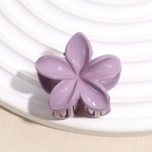 Détail d'une pince à cheveux fleur mauve mate avec ressort mécanique sur socle blanc