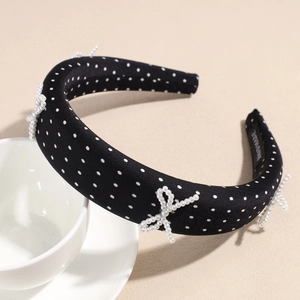 Close-up of black polka dot headband with three white imitation pearl bows and tag
