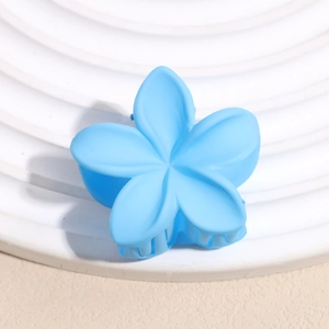 Gros plan d'une pince à cheveux fleur bleu ciel mat sur un piédestal blanc