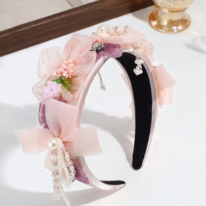 Détail d'un serre-tête fleurs en tissu rose avec perles et cristaux sur un support
