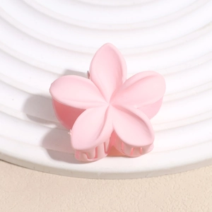 Détail macro d'une pince à cheveux fleur rose mate sur un support blanc texturé minimaliste