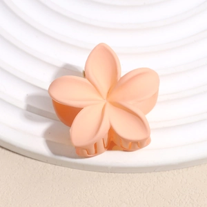 Gros plan sur une pince à cheveux fleur mate pêche sur un support décoratif blanc
