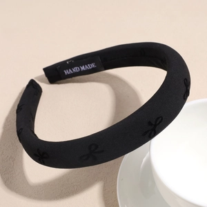 Detail of black sponge headband with embroidered bows and 'HAND MADE' label