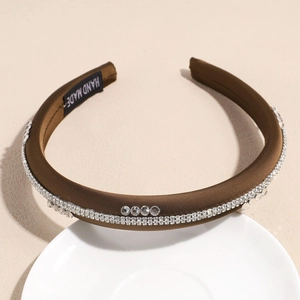 Détail du bandeau en satin marron avec double rangée de strass sur une assiette blanche