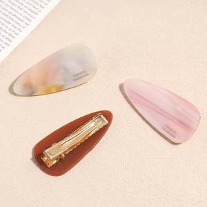 Three acetate marble duckbill hair clips in pink and iridescent colors with gold metal base