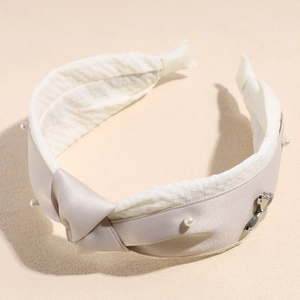 Detail of cream satin knotted headband featuring white pearls and a silver metal charm