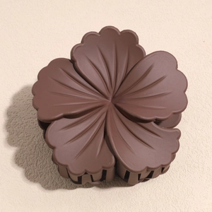 Detail of dark brown matte flower hair claw clip with textured petals on beige background