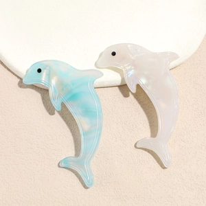 Dolphin-shaped acetate hair clips in marble blue and pearlescent white on stone tray