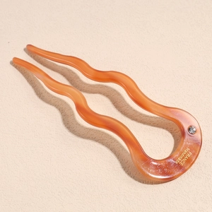 Detailed view of U-shaped amber hair pin with wave design and rhinestone accents