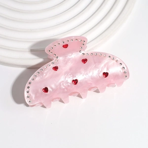 Pinza per capelli in acetato rosa con strass a cuore rossi su vassoio bianco elegante