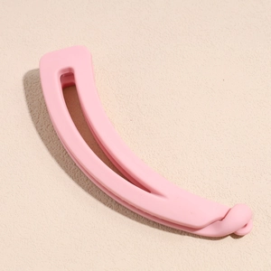 Gros plan d'une pince banane rose mat pour femmes sur un fond beige texturé élégant