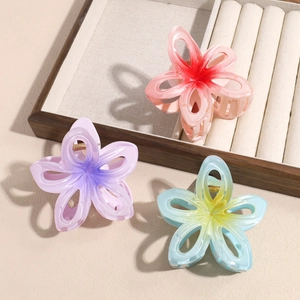 Trois pinces à cheveux à fleurs dégradées rose, violet et bleu sur un plateau de bijoux en bois