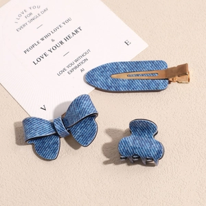 Three-piece denim blue hair clip set including bow and claw clips on a cream surface