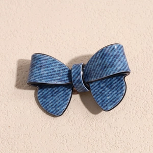 Detail view of denim blue bow hair clip with black border on textured beige wall