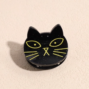 Close-up of a black cat hair clip with silver glitter and yellow facial details