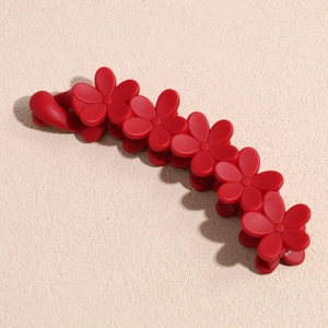 Détail d'une pince à cheveux banane à fleurs rouge foncé mat sur surface en pierre texturée