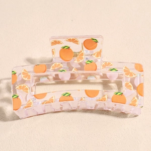 Detail of a square transparent pink hair claw clip featuring orange fruit patterns