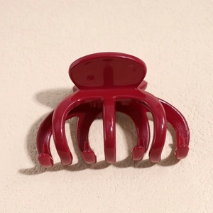 Macro view of a glossy wine red claw clip on a textured beige surface background