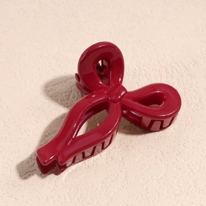 Close-up of a burgundy bow-shaped hair claw clip with glossy finish on beige surface
