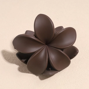 Detail view of a matte chocolate brown flower hair claw clip on a beige textured background