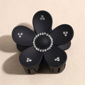 Détail d'une pince à cheveux fleur noire avec strass brillants sur des pétales mats