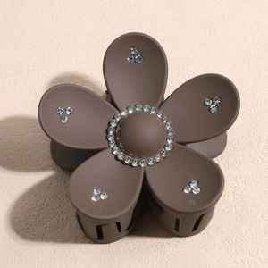 Détail d'une pince à cheveux fleur marron mat avec strass blancs sur fond beige neutre